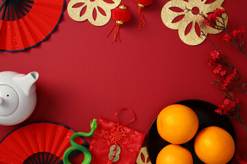Chinese New Year 2025 flat lay composition with festive decorations, teapot, paper fans, envelopes, cherry blossoms on red background.