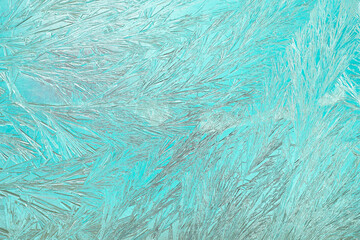 A close-up view of intricate frost crystals forming unique patterns on a vibrant aqua background. Perfect for winter themes and artistic design projects. Frosty windowpane