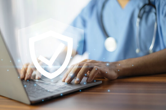 Doctor typing on a laptop with a glowing shield icon, symbolizing cybersecurity and data protection in healthcare. - Powered by Adobe