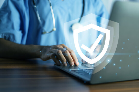 Doctor typing on a laptop with a glowing shield icon, symbolizing cybersecurity and data protection in healthcare.