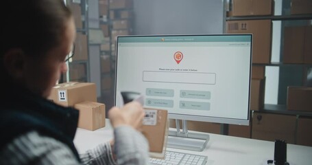 Female Postal Warehouse Employee Scans Code on Cardboard Box with Barcode Scanner, Monitors Package Information. PC Screen Shows Delivery Tracking Software to Check Parcel Routing. Dolly Shot Close Up - Powered by Adobe