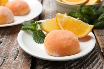 Plate with tasty mochi, cut orange and mint on wooden table, closeup