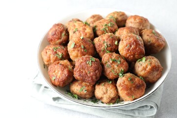 Tasty cooked meatballs with green onion in bowl on white table, closeup