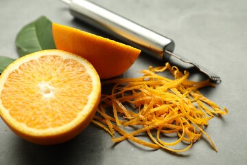 Orange zest, zester tool and fresh fruit pieces on gray textured table, closeup