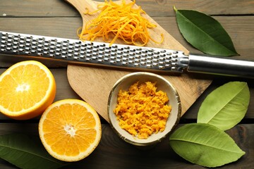 Orange zest, grater and fresh fruit pieces on wooden table, flat lay