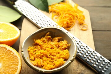 Orange zest, grater and fresh fruit pieces on wooden table, closeup