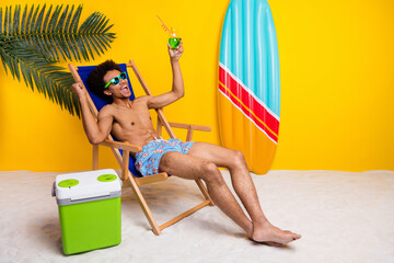 Cheerful young man relaxing on a tropical resort with a refreshing drink. He is lounging on a beach chair, enjoying summer vibes.