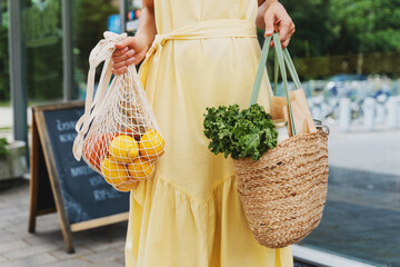 Woman holding bags with fresh organic food on storefront background of zero waste shop.