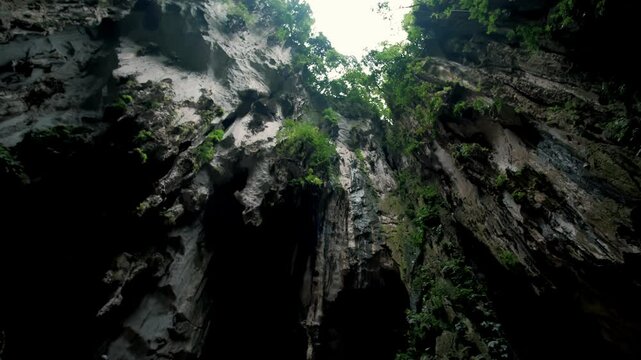 Sunlight streaming through batu caves entrance, highlighting verdant tropical foliage surrounding limestone cavern opening in malaysia