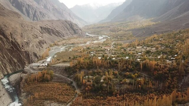 Aerial view of the serene Gilgit River flowing through a picturesque valley surrounded by majestic mountains and remote village homes, Gupis, Pakistan.
