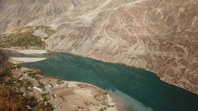 Aerial view of the beautiful Gilgit River winding through the serene valley surrounded by majestic mountains and picturesque village, Gupis, Pakistan.