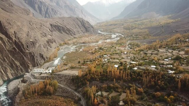 Aerial view of serene Gilgit River flowing through a picturesque valley surrounded by majestic mountains and a rural village, Gupis, Pakistan.