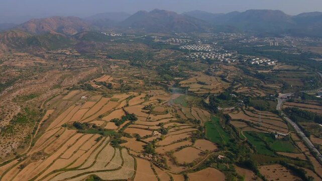 Aerial view of the Dharmarajika Stupa ruins surrounded by scenic farmland and mountains in the Pothohar region, Taxila, Pakistan.