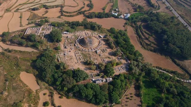 Aerial view of dharmarajika stupa and ancient ruins surrounded by green fields and trees, Taxila, Pakistan.