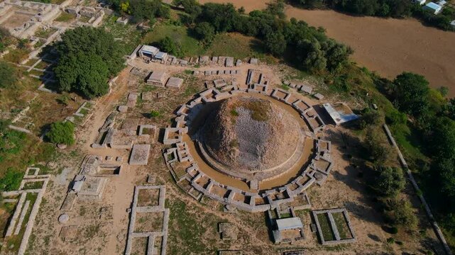 Aerial view of dharmarajika stupa ruins with ancient stone structures and surrounding fields, Taxila, Pakistan.