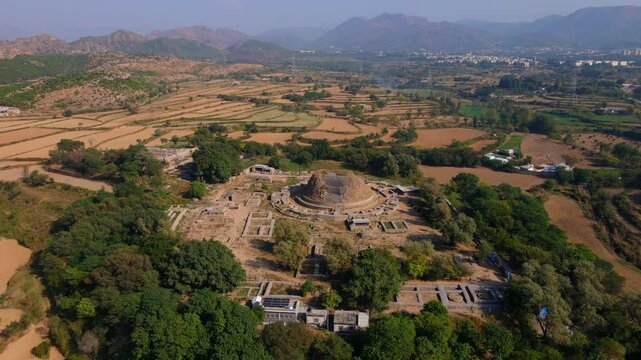 Aerial view of dharmarajika stupa ruins amidst lush green landscape and scenic mountains, Taxila, Pakistan.