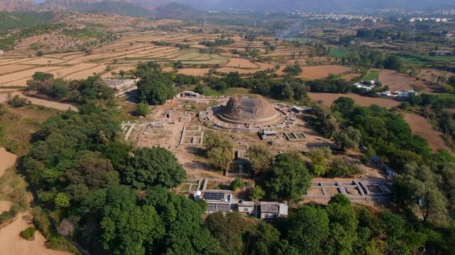 Aerial view of dharmarajika stupa ruins surrounded by beautiful fields and mountains, Taxila, Pakistan.