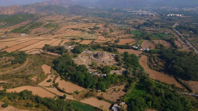 Aerial view of Dharmarajika Stupa ruins surrounded by green fields and countryside, Taxila, Pakistan.