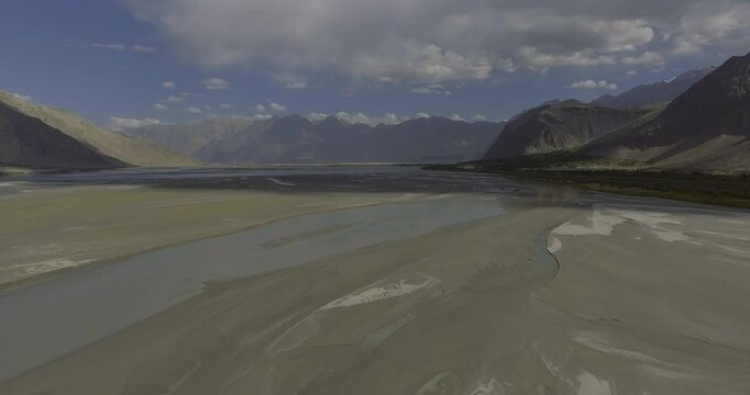 Aerial view of the majestic Indus River winding through a serene valley surrounded by rugged mountains and clouds, Gilgit Baltistan, Pakistan.
