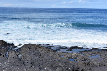 White waves blue ocean and lava rocks on canary coast