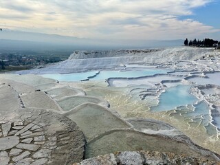 Naklejka premium Pamukkale's travertine terraces with turquoise thermal pools, ancient ruins, and a dramatic sky