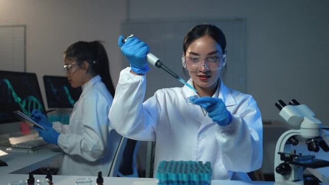 Asian female scientist dripping blue liquid into microplate using micropipette in laboratory