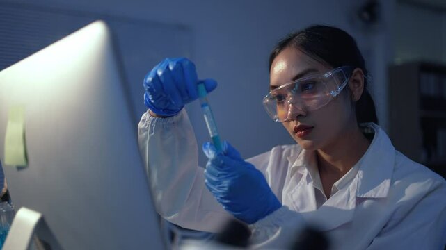 Asian female scientist wearing lab coat and gloves analyzing a test tube with blue liquid in a laboratory