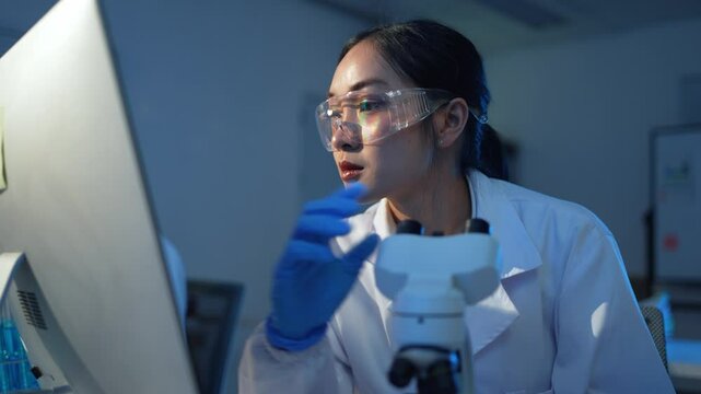 Female scientist wearing lab coat working intently with precision, analyzing scientific data through advanced microscope in modern research laboratory setting