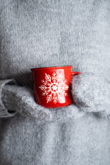 A woman in a warm gray sweater holds a mug in her hands. Close-up of female hands holding a cup of...