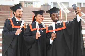 Happy African American students taking selfie with cell phone on their graduation day