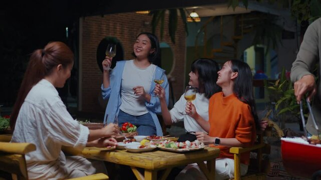 Friends enjoying wine and delectable cuisine during vibrant nighttime gathering, radiating happiness while sharing memorable moments in outdoor garden setting