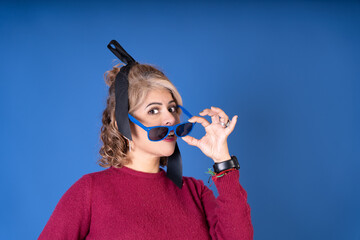 Curious woman lowering sunglasses making a funny face on blue background