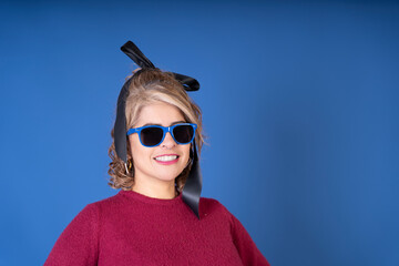 Smiling woman wearing sunglasses and black ribbon posing on blue background