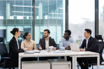 Diverse business colleagues and partners sitting at tables in meeting room, people happily discussing new startup and business investment, company employees with boss in business suit.
