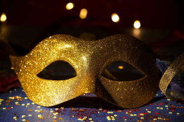 Beautiful carnival mask and confetti on dark background with blurred lights, closeup
