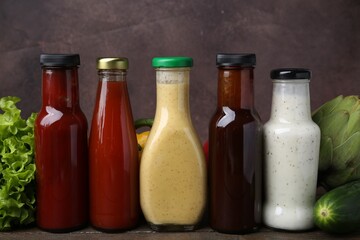 Tasty sauces in glass bottles and fresh products on wooden table, closeup