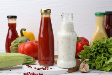 Tasty sauces in glass bottles and fresh products on white wooden table, closeup