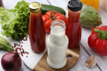 Tasty sauces in glass bottles and fresh products on white wooden table, closeup