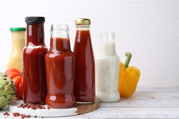 Tasty sauces in glass bottles and fresh products on wooden table, closeup. Space for text