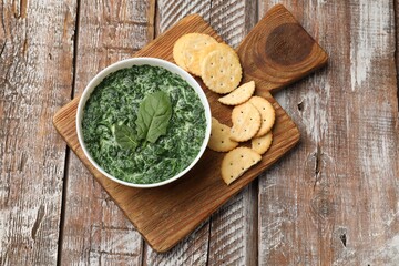 Delicious spinach sauce in bowl and crackers on wooden table, top view