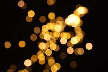 Blurred view of golden lights on black background, bokeh effect