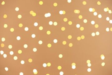 Blurred view of golden lights on light background, bokeh effect