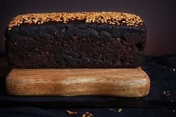 Fresh brown bread with grains and sesame on a wooden board on a dark background