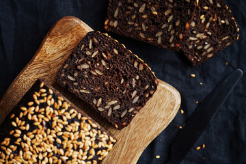 Fresh brown bread with grains and sesame on a wooden board on a dark background