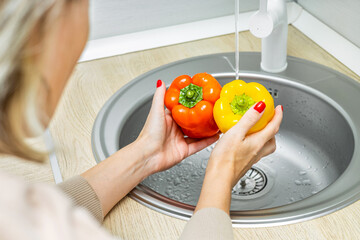 woman washing bell peppers in kitchen sink. housewife washes vegetables in the kitchen. bell pepper in the kitchen. woman holding bell peppers in her hands