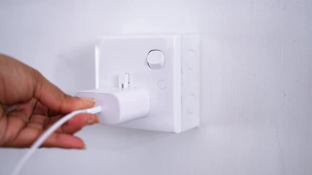 A close-up of removing the phone charger and cable from the electrical outlet on the wall and switching it off, captured in high-quality 4K video footage. Ideal for technology, charging.