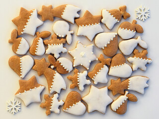 Decorated gingerbread cookies of various shapes on a white background with white snowflakes. Christmas baking