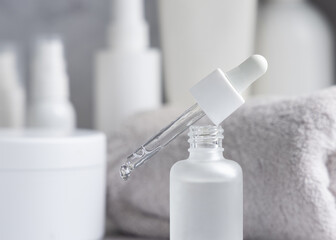 Pipette set on a glass dropper bottle on white marble near cosmetics and towel close up