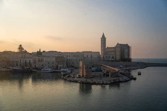 View of beautiful Catholic cathedral by the scenic harbor with fishing boats at sunset, Trani, Italy.