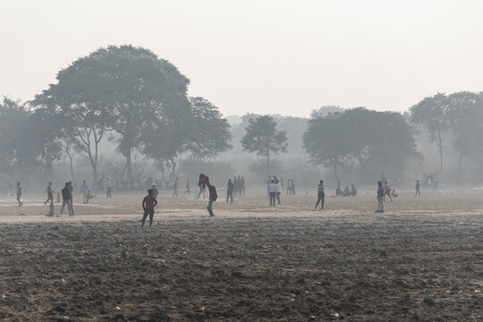 Agra, India - 01 December 2024: View of people playing cricket in a foggy rural field surrounded by trees, Agra, India.